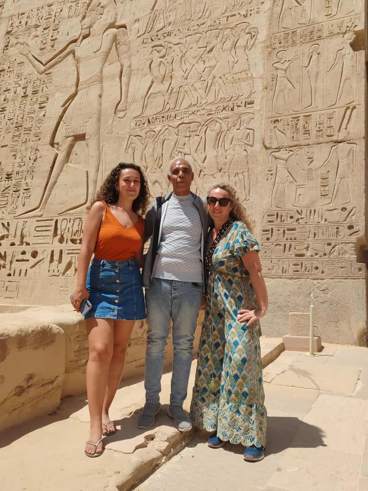 Two travelers posing with their guide beside carved temple reliefs in Luxor