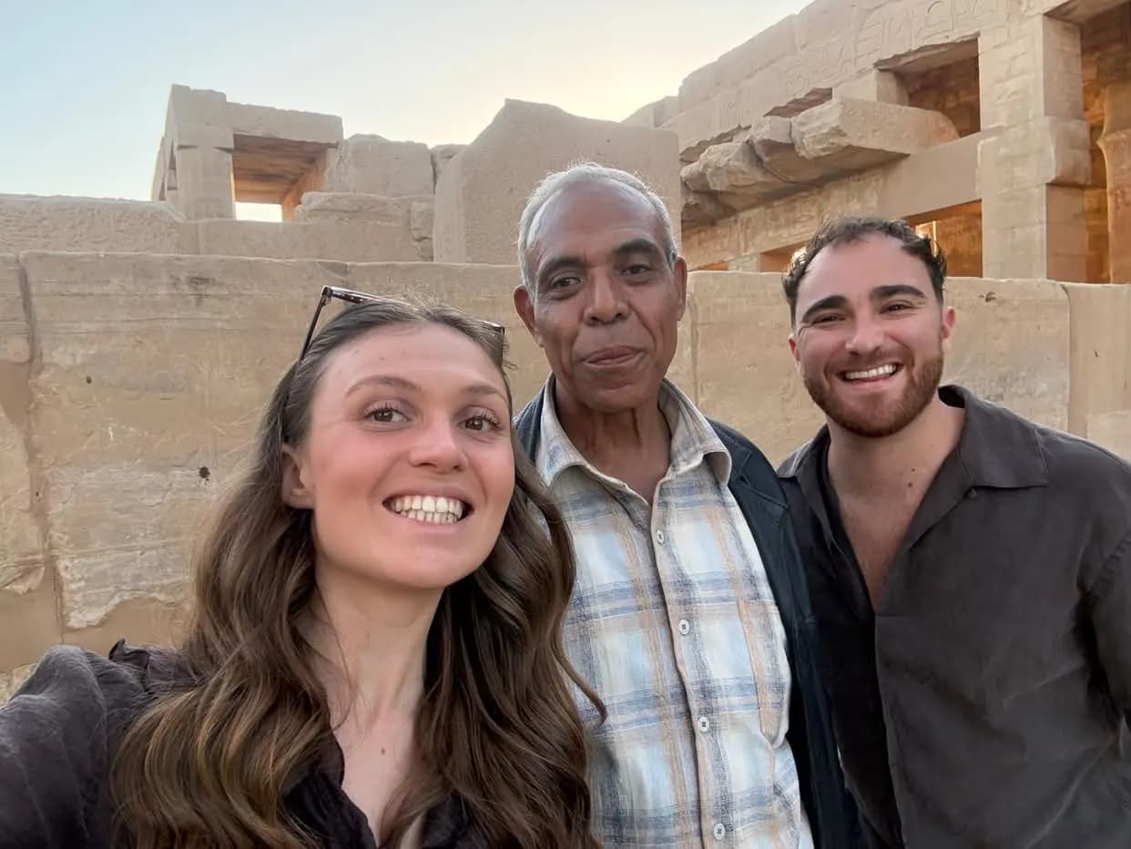 Two travelers and a local guide smiling for a selfie at a temple at sunset