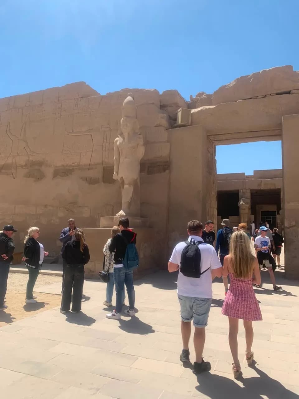 Tourists walking past a colossal pharaoh statue at Karnak Temple, Luxor