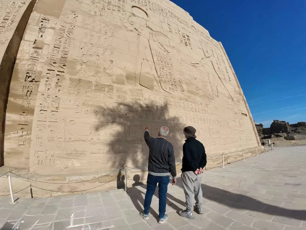 Visitors viewing carved reliefs on a temple wall at Medinet Habu, Luxor