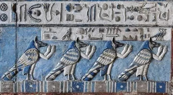A painted relief of falcon-headed figures on a blue temple wall, Dendera